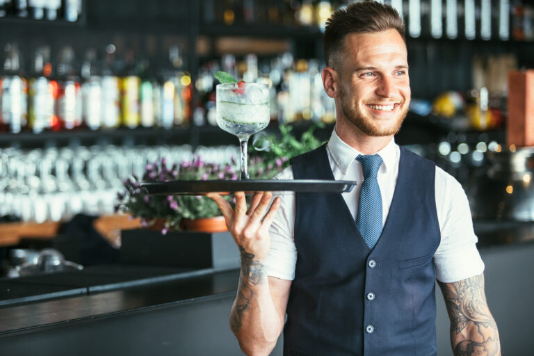 Smiling elegant waiter is holding a tray with a decorated cocktail ready to serve